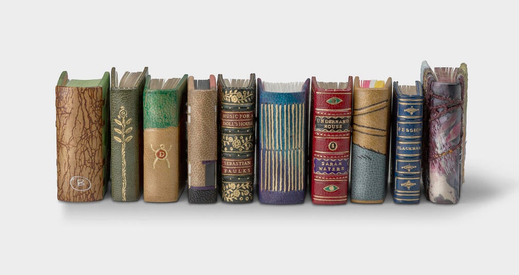 A selection of ten of the new miniature books, lined up so that their spines are visible, which shows the variety of design styles and colours used by the binders. 