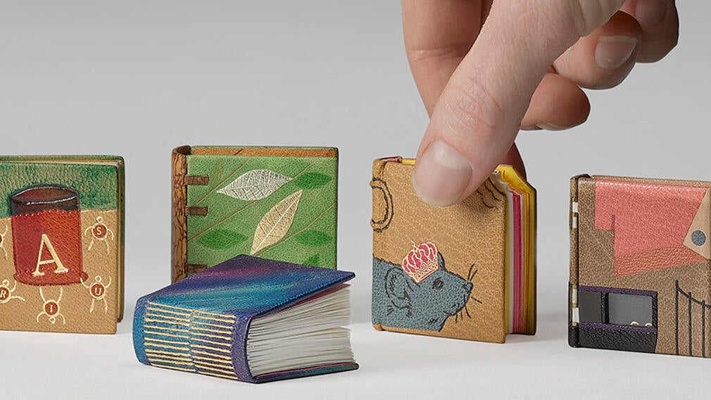 A selection of miniature books with a hand about the pick one up.