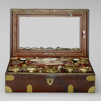 A mahogany and brass-mounted box, lined with tooled red leather and containing a French silver-gilt, ivory, mother of pearl and cut-glass travelling service, the pieces packed into fitted leather trays. Many pieces are engraved wi