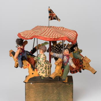 Miniature toy merry-go-round with red and white striped cotton canopy with Union flag; from which are suspended six wooden painted horses each with wooden and textile rider. On green painted wooden base containing mechanism and turning hand