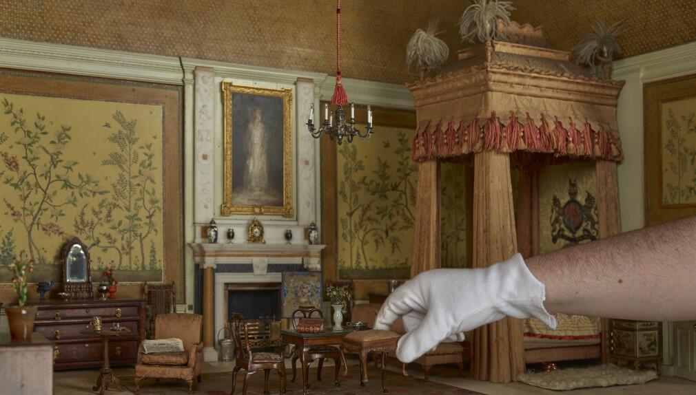 The King's Bedroom in Queen Mary's Dolls' House with a hand reaching in to pick up furniture