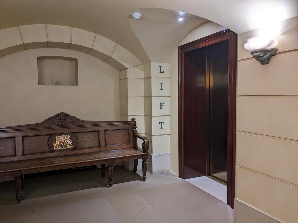 A space with a large wooden bench and the access to the lift