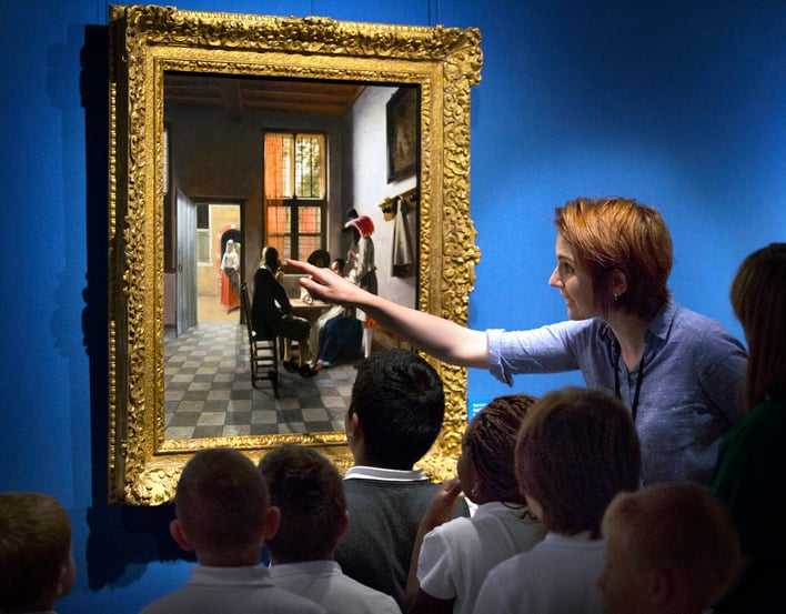 Small group of children with teacher looking closely at a painting on gallery wall