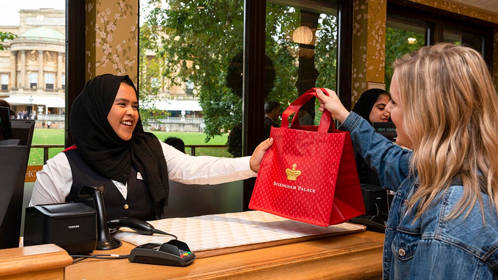 A woman at a cashier desk hands a customer a red bag of her purchases