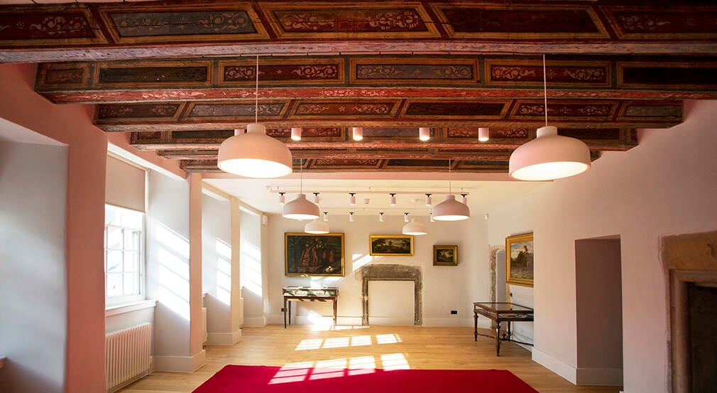 The interior of a room with old wooden beams, white walls and paintings on the wall.