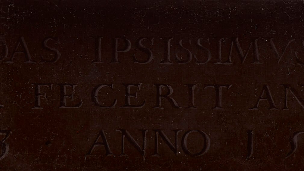 A latin inscription painted on a painting. The background is brown.