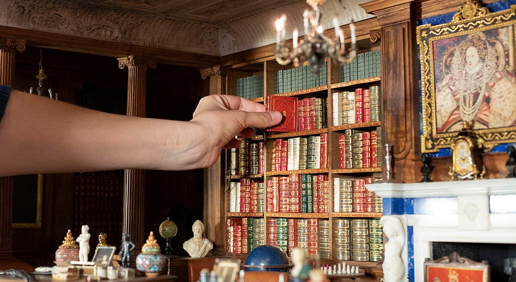 A miniature library with a hand reaching to grab a book.