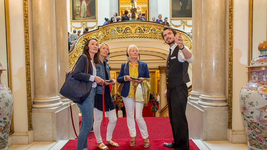 A warden showing visitors the Grand Staircase at Buckingham Palace.