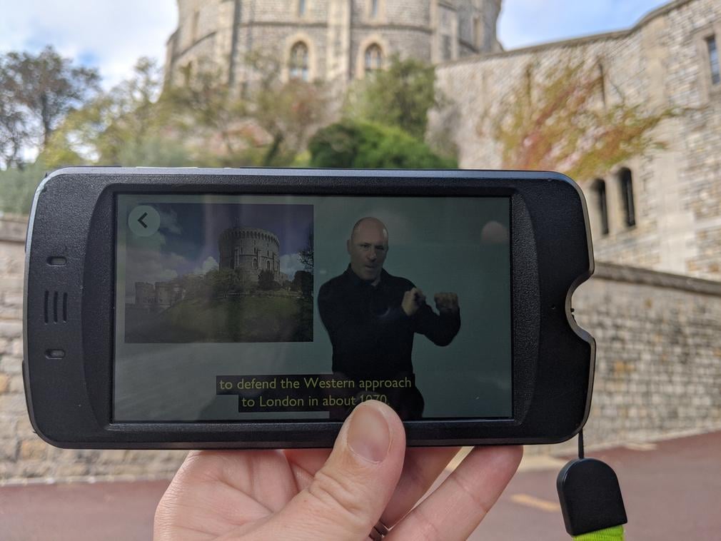 A hand holding a multimedia device, like a mobile phone, in front of the Round Tower