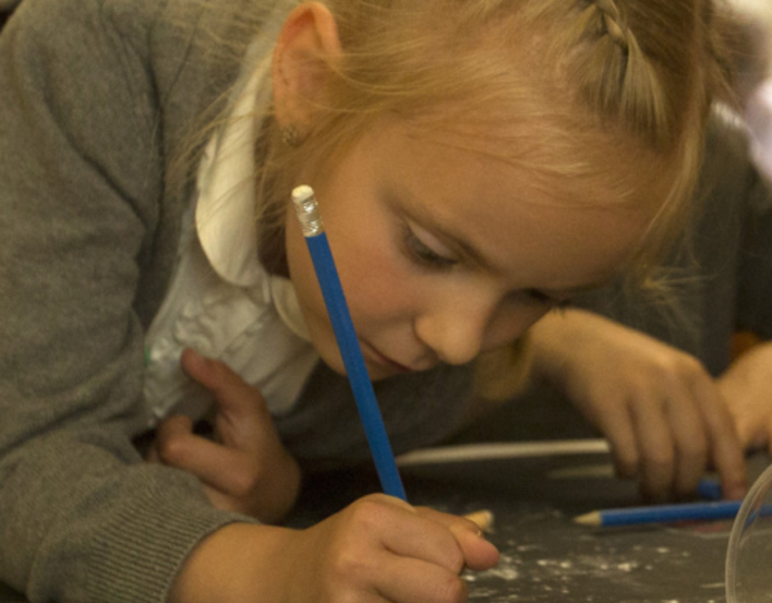 A girl leaning over paper and drawing with a pencil