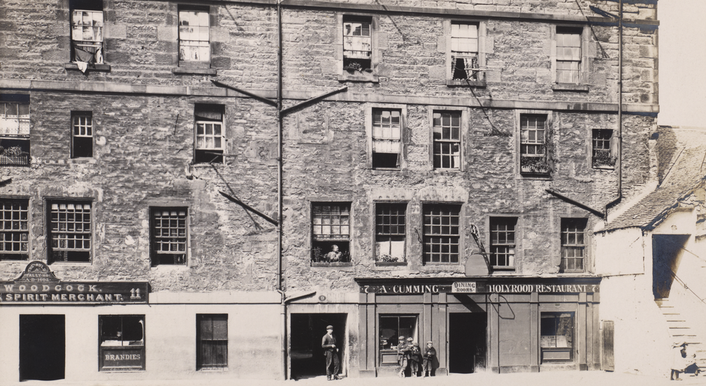 A black and white photo of building in 1903. A man and children stand outside the buildings.